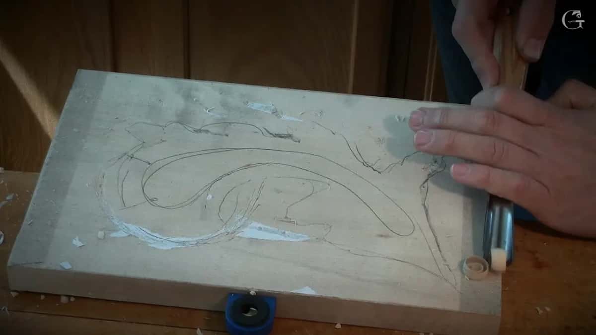 Outline before the first pass Leaf outline traced in pencil onto a plain board with the gouge that will open it lying alongside