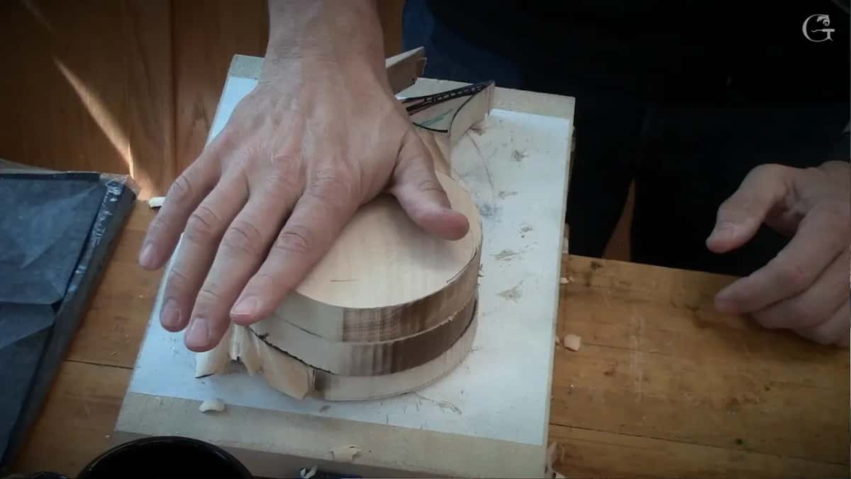 A hand pressing glued basswood layers flat with glue lines showing