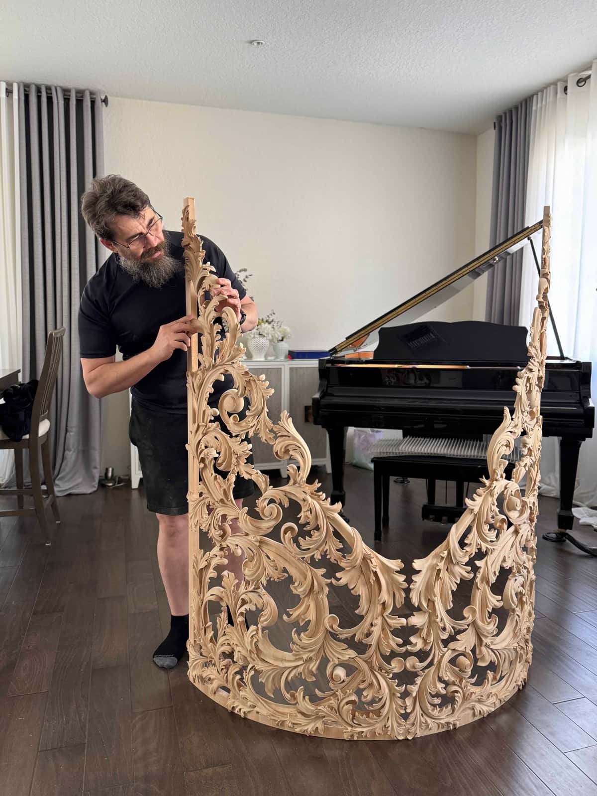 A bearded man holds a large wood panel carved with flowing acanthus leaf scrolls in a living room