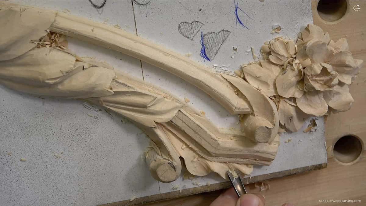 Curved pale carving in progress with an acanthus scroll and a peony, chips scattered across the backing board