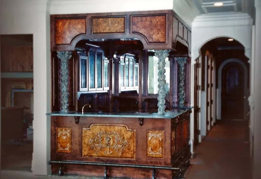 Burl panels and twisted columns make up a finished home bar, and a carved cartouche sits applied to the centre panel below the counter where no carver could ever have carved into that figured veneer