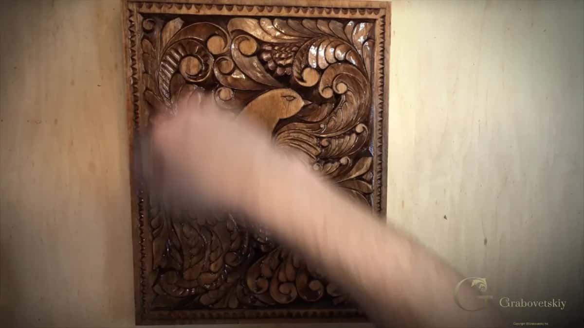 Hand wiping food grade oil across a finished dark carved board, the oil soaking into the surface