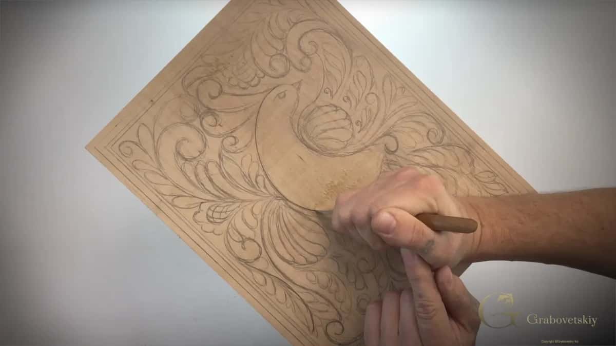 Carving knife tracking the pencil outline of a bird on a board at a low angle, worked slowly