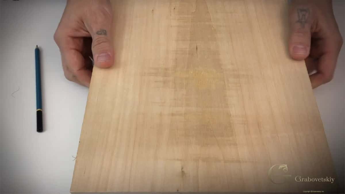Bare basswood board resting on the bench with a pencil beside it, the best wood for beginners to carve