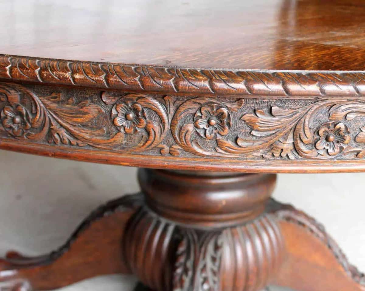 An acanthus scroll with small five petal flowers carved into the solid oak apron of a dark antique table