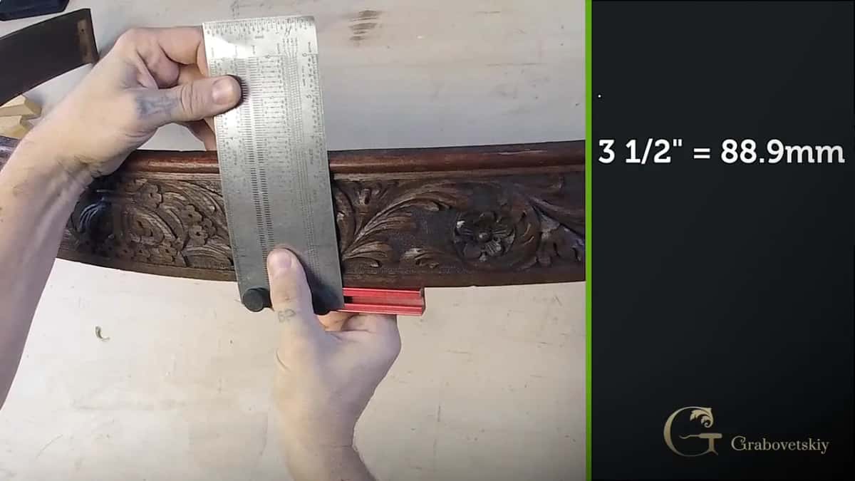 Measuring an antique carved apron with a steel rule A wide steel rule held across a dark antique carved apron