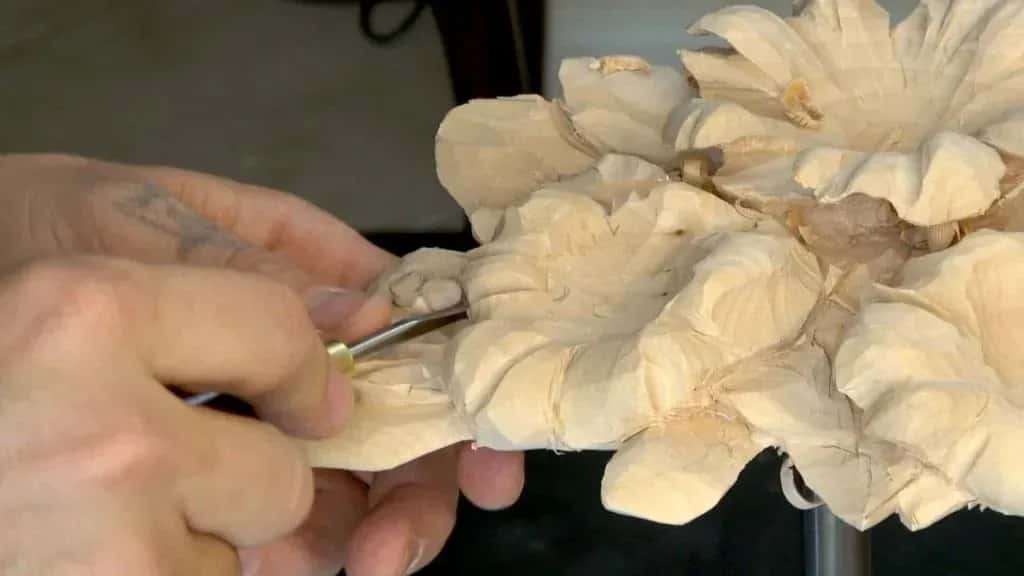 A small gouge worked along the edge of a carved basswood flower, running downhill with the grain