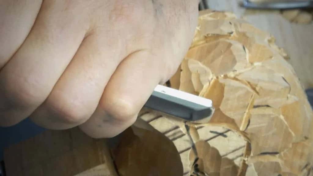 Close over a hand cutting faceted flower forms, the tool almost touching the lens