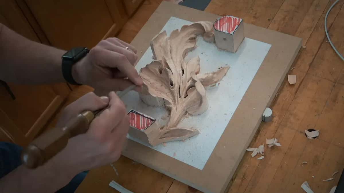 Both hands driving one long gouge across a half finished acanthus with red depth marks