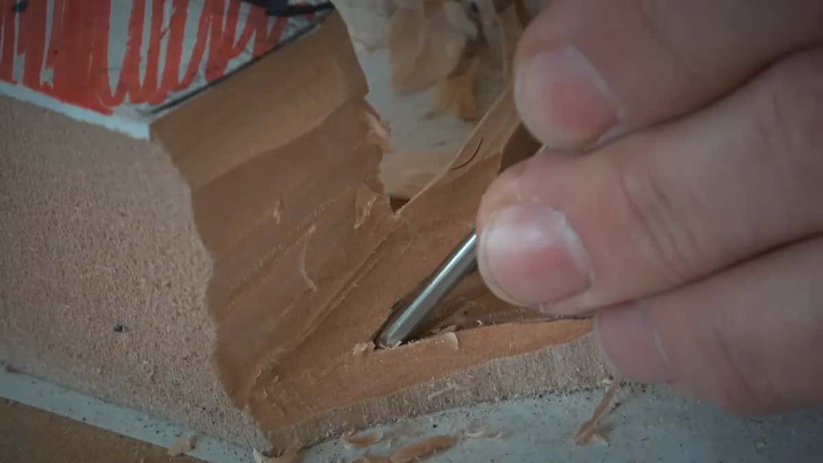 Tip of a small carving gouge lifting one curl of basswood from a tight corner