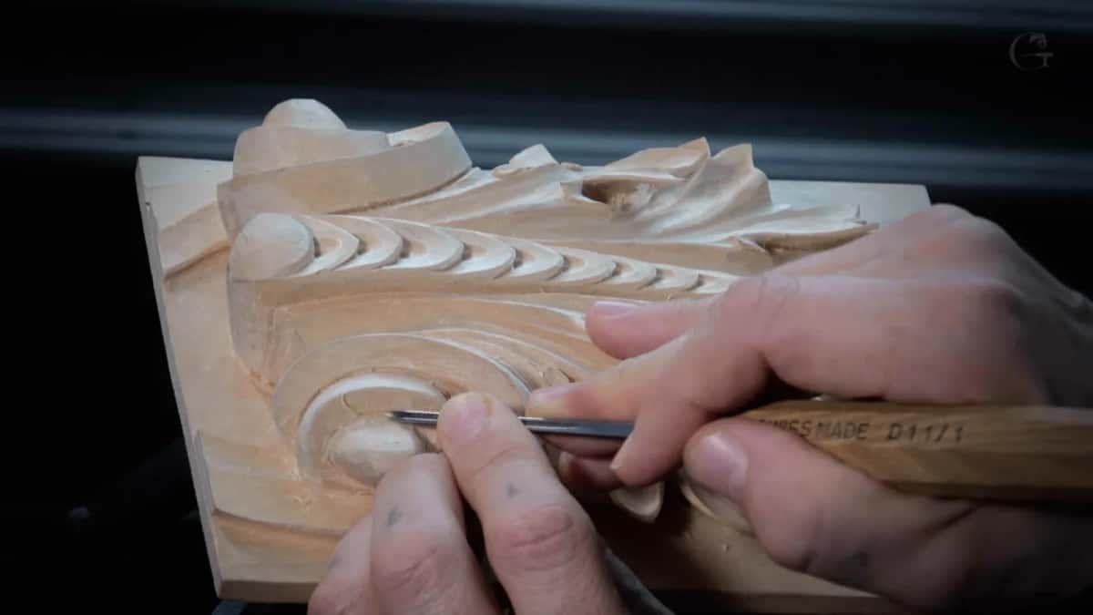Working the lower volute Gouge steered around the deep lower volute, chips heaped beside the board and the leaves above still papered over