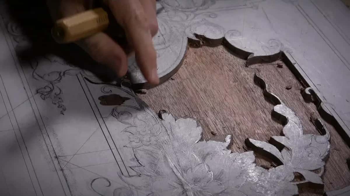 A chisel and mallet lower the ground to bare dark walnut beside the drawn ornament on a big panel.