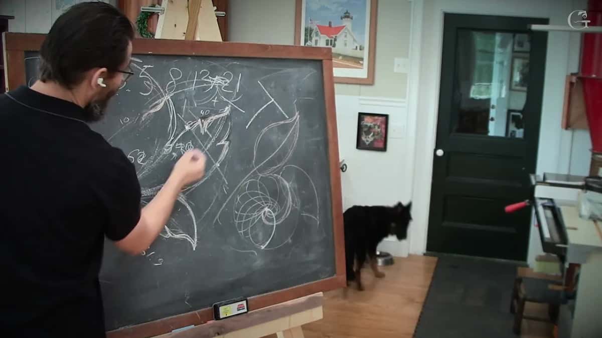Drawing an acanthus on the shop chalkboard Me at the chalkboard drawing a leaf under the number row, a letter T in the corner, and the dog waiting by his bowl