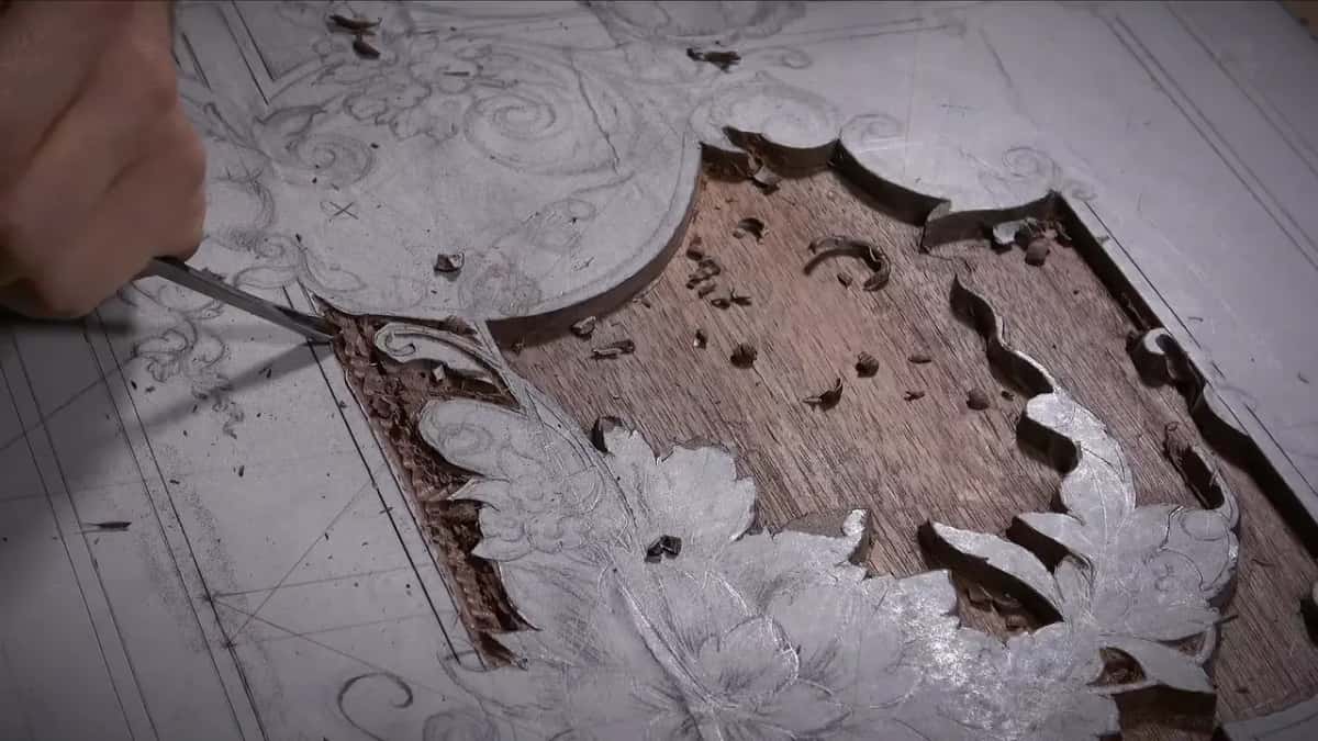 The ground is cleared to bare mahogany around a chalked design, chips scattered over the panel.