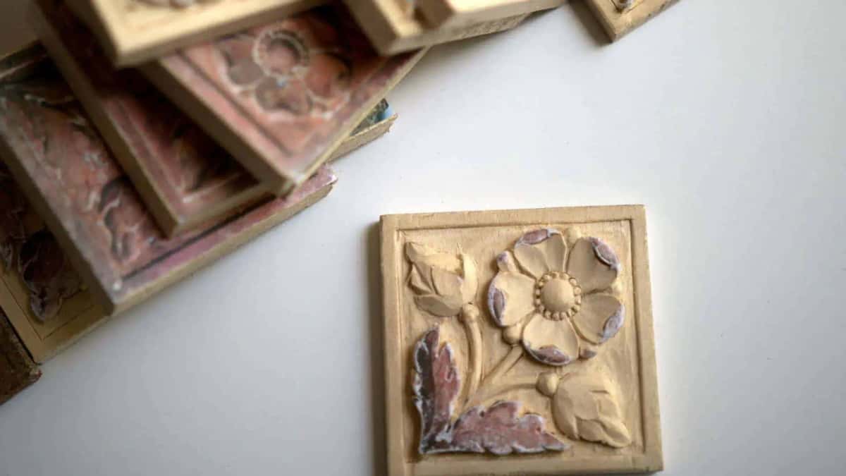 Fresh pale carved flower tile in front of a stack of older painted tiles with worn pink and red paint