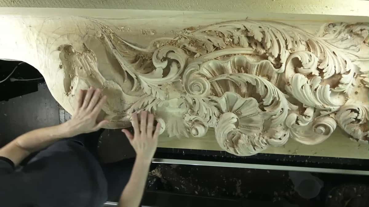 Two hands resting on a long carved basswood frieze, chips still lying on the surface