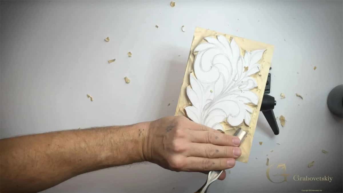 A flat gouge clearing the raw ground beside a leaf that is still only white paint and pencil