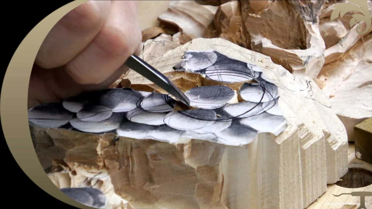 Paper pattern of a grape cluster glued down on the basswood blank, with a chisel taking the first stop cut through the paper and the drawn berries
