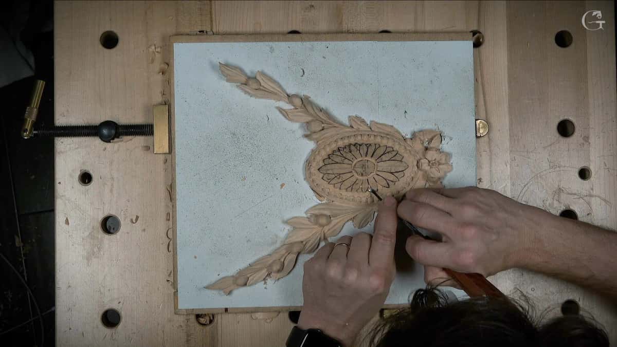 An oval rosette being laid out and carved on a benchtop, seen from directly above