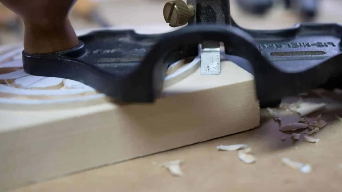 Router plane set on a blank with its blade cutting the ground level around a round carving