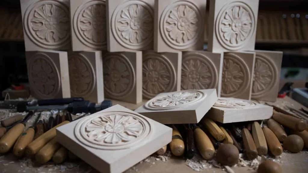 A row of carved antique rosettes standing on the bench with gouges scattered in front of them