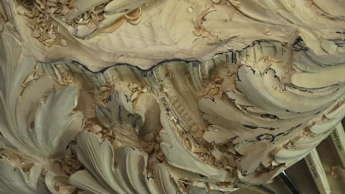 Deeply carved acanthus leaves buried in fresh chips, charcoal layout lines still crossing them, a gouge at the edge.
