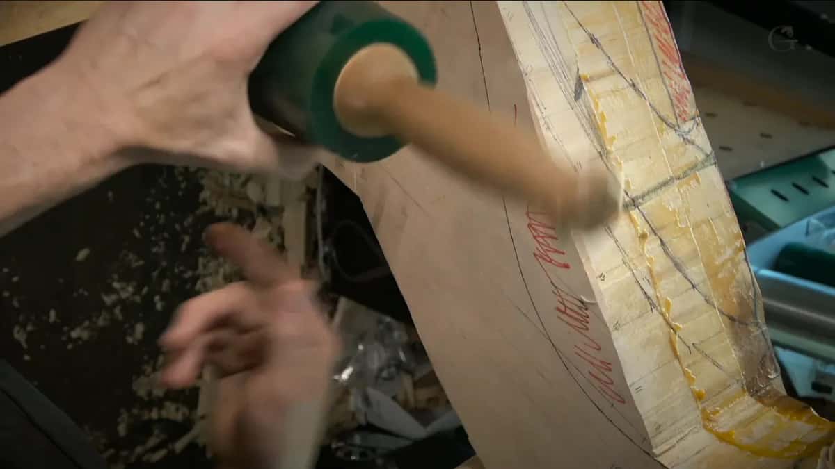 A green-faced mallet in the hand above a laminated blank hatched in red marker and numbered in pencil.