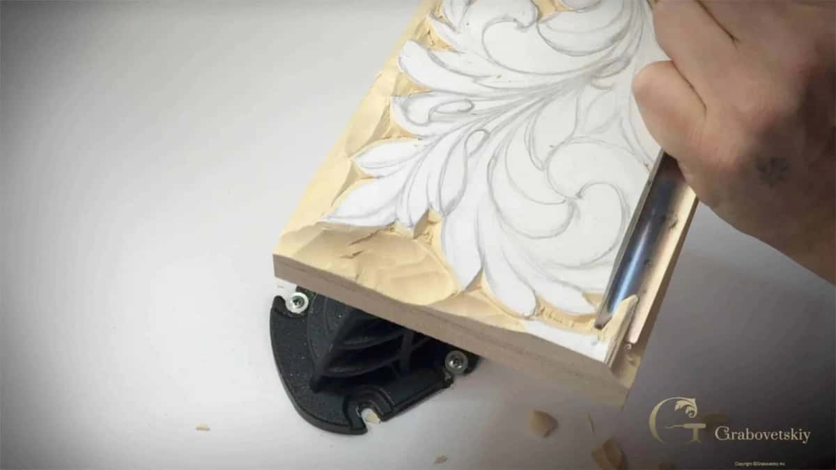 A long bladed tool riding the pencil outline of an acanthus panel at an angle