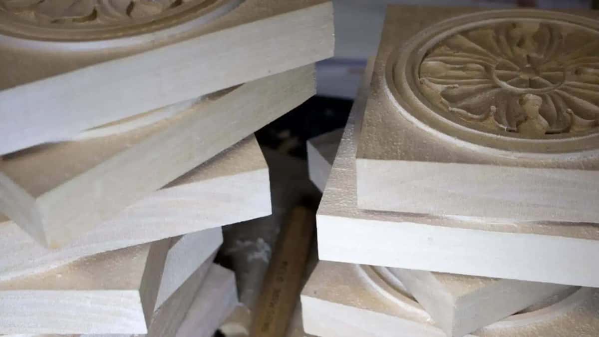 Stack of sawn pale carving blanks seen edge on with one finished carved rosette resting alongside