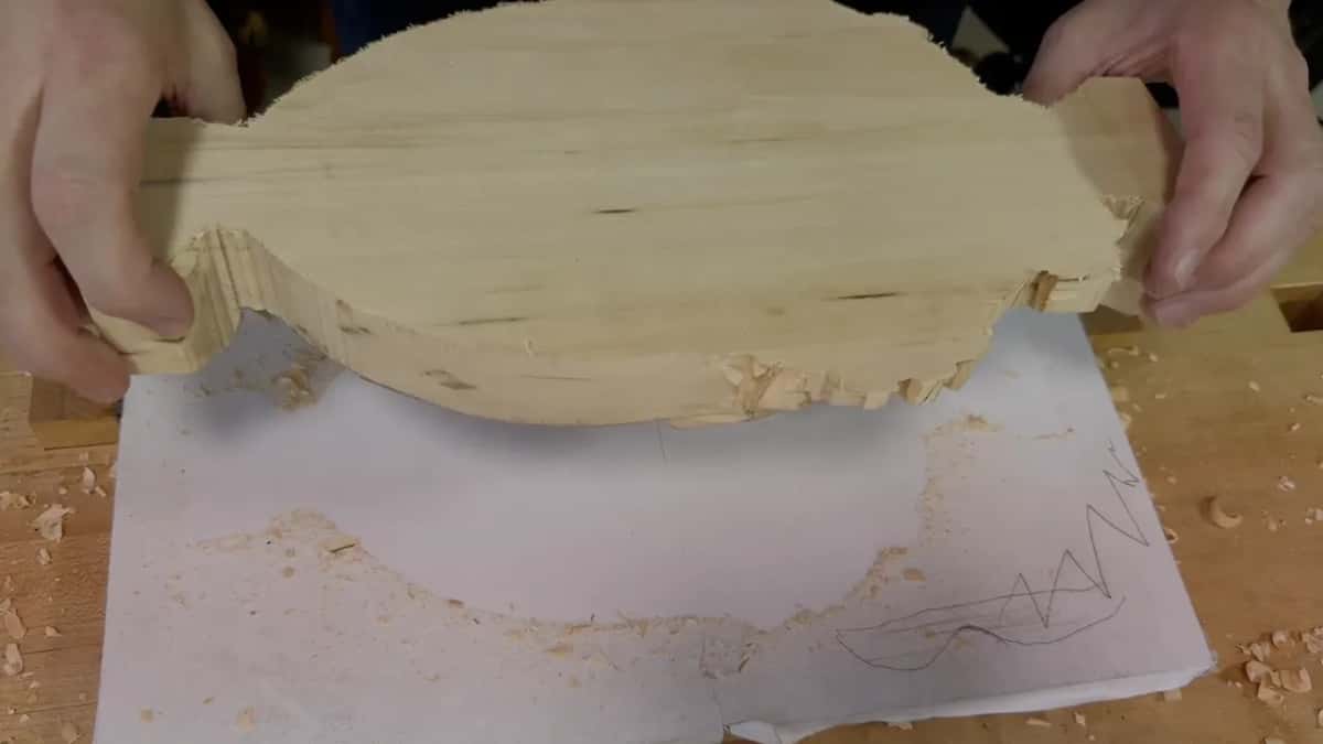 Tray off the board Both hands lifting a finished tray free of the board it was carved on, the paper drawing still lying underneath it