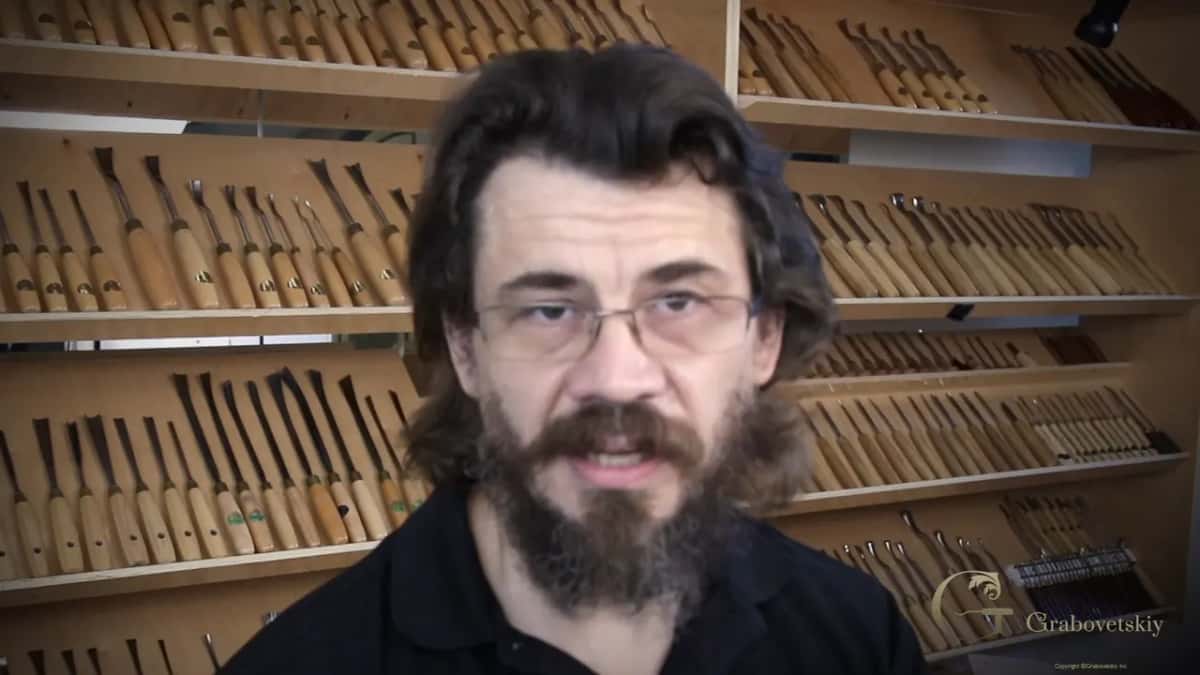 Alexander Grabovetskiy speaking to camera in front of the shop wall of carving gouges