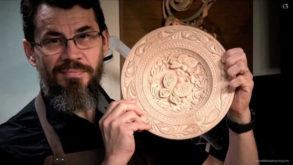 The finished butterfly plate Alexander Grabovetskiy holding up a round basswood plate carved with butterflies inside a beaded ring and a leaf border