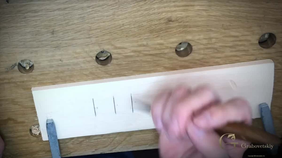 Three pencil marks on a clamped basswood board with the knife making the angled pass five millimetres out