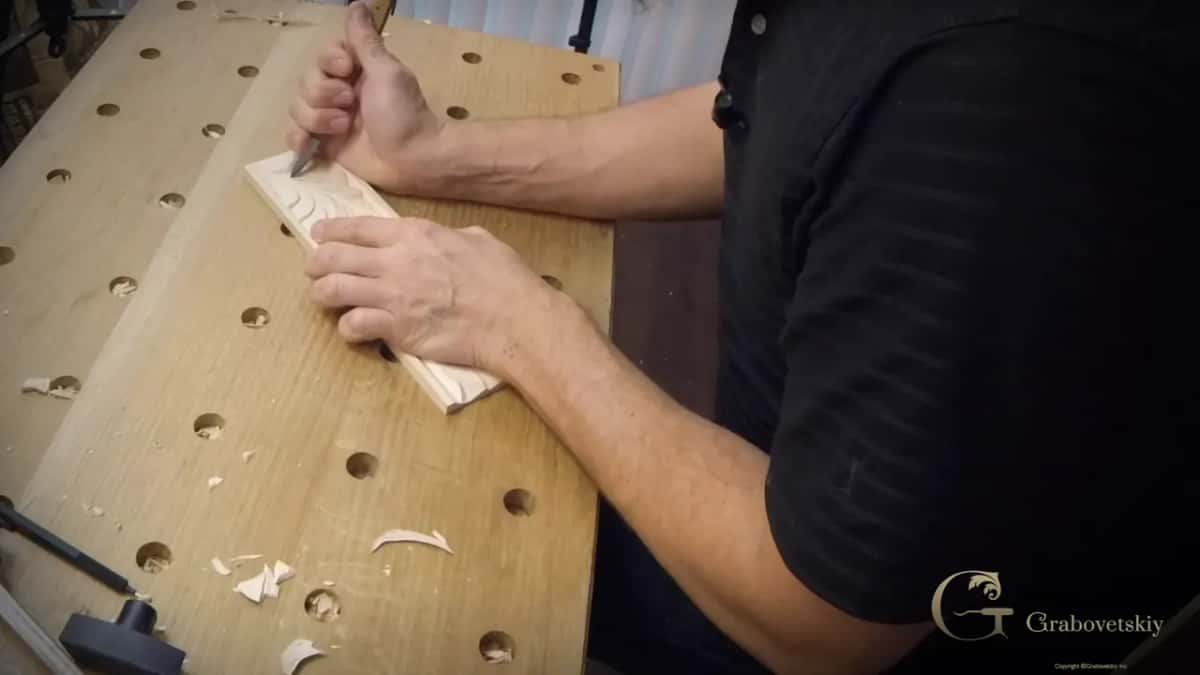 Carving the leafy design with the knife while chips gather across the bench