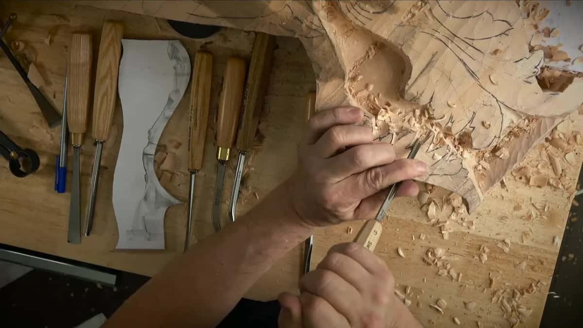Two hands on one gouge, working down the curve of the hollow, a paper template lying on the bench