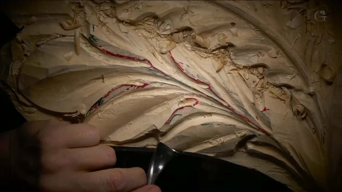 Fingers hold a bent tool against the outer edge of the new leaf, lit from one side