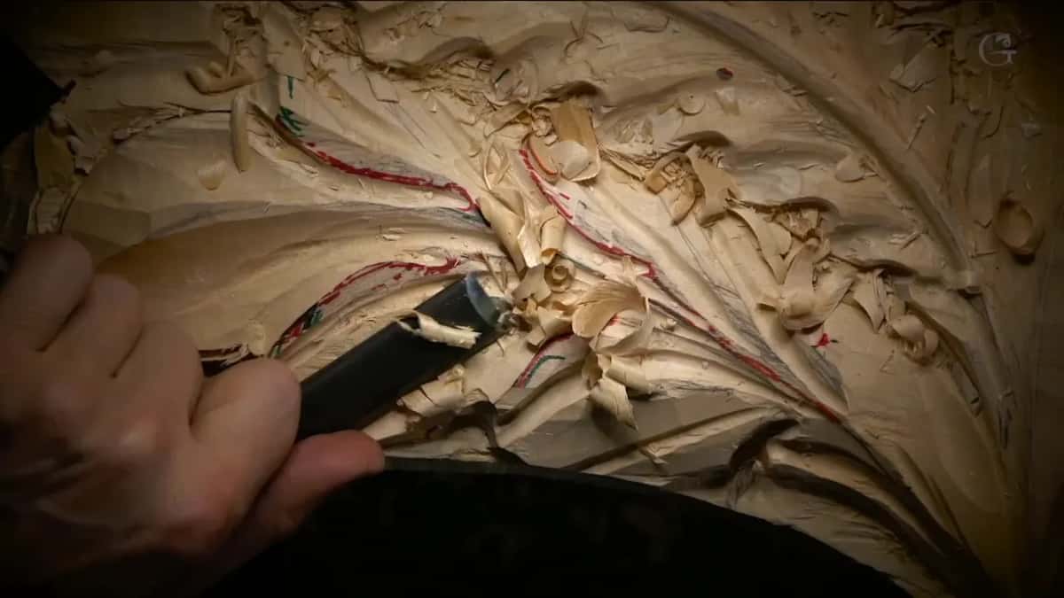 A dark handled gouge sits in a concave, surrounded by curled chips and red marker lines