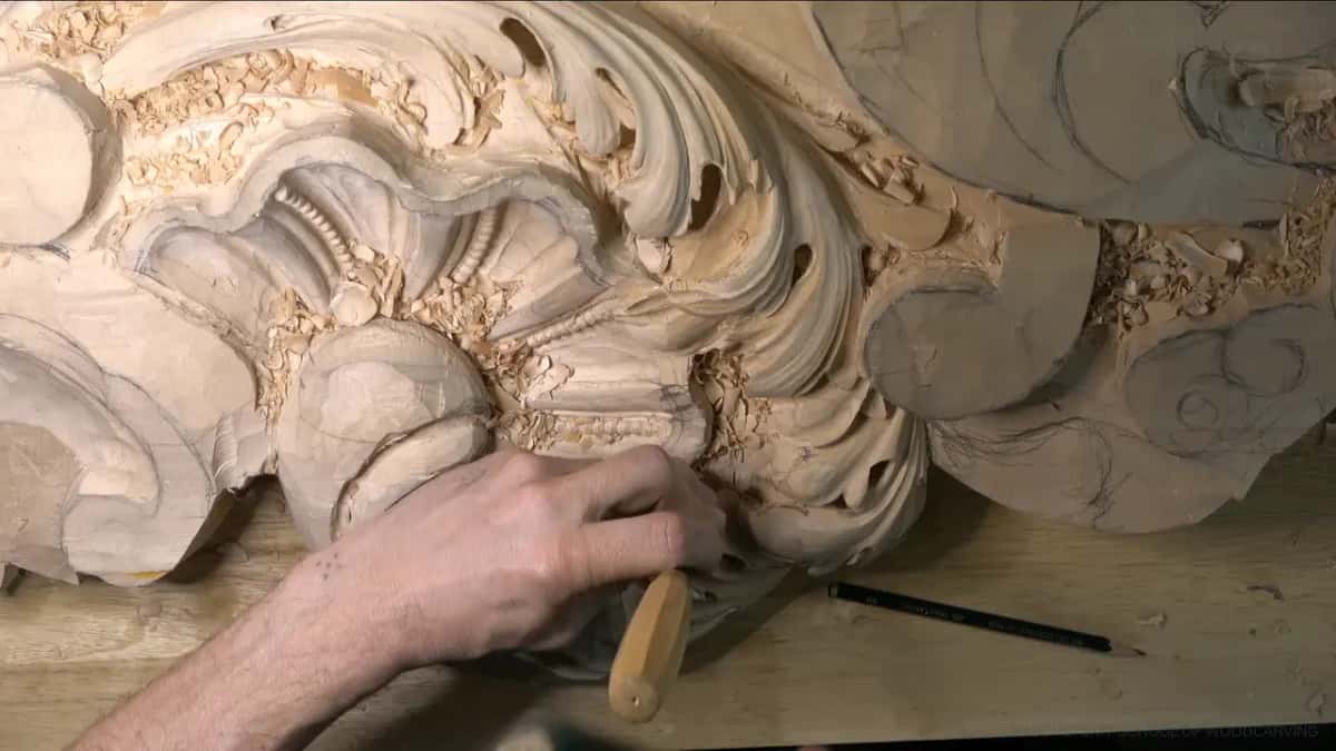 Round handle in the fist, edge buried in a curl next to the shell, pencil resting on the bench.