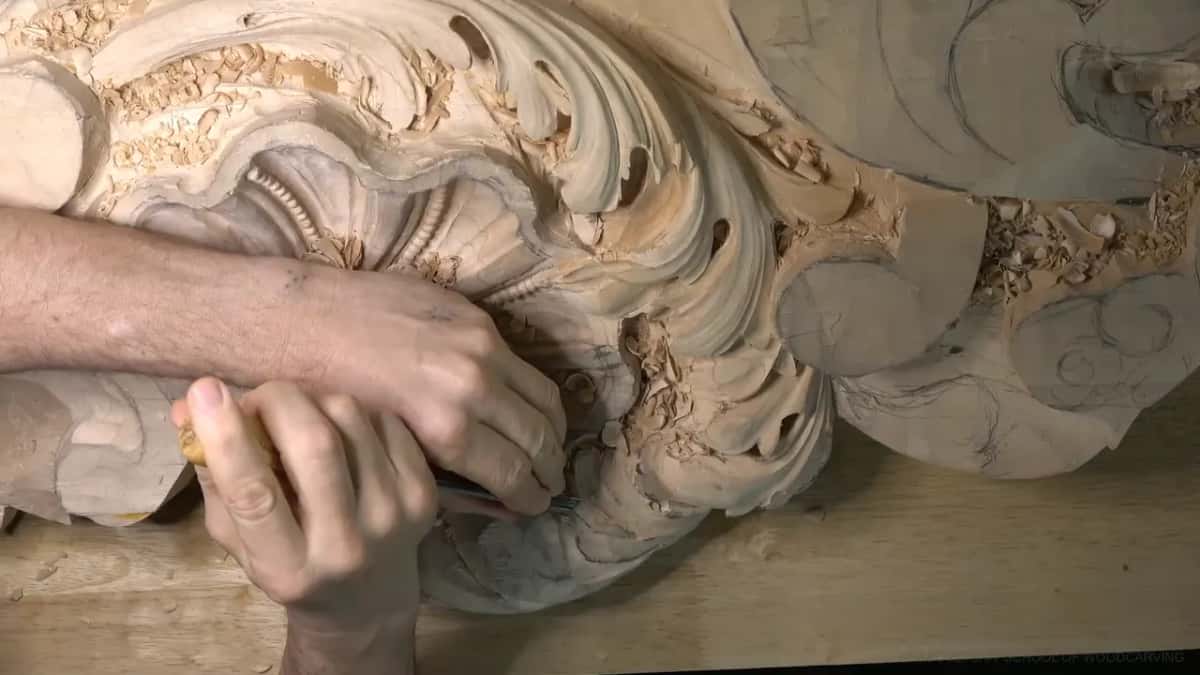 Two hands guide a yellow-handled gouge under the shell.