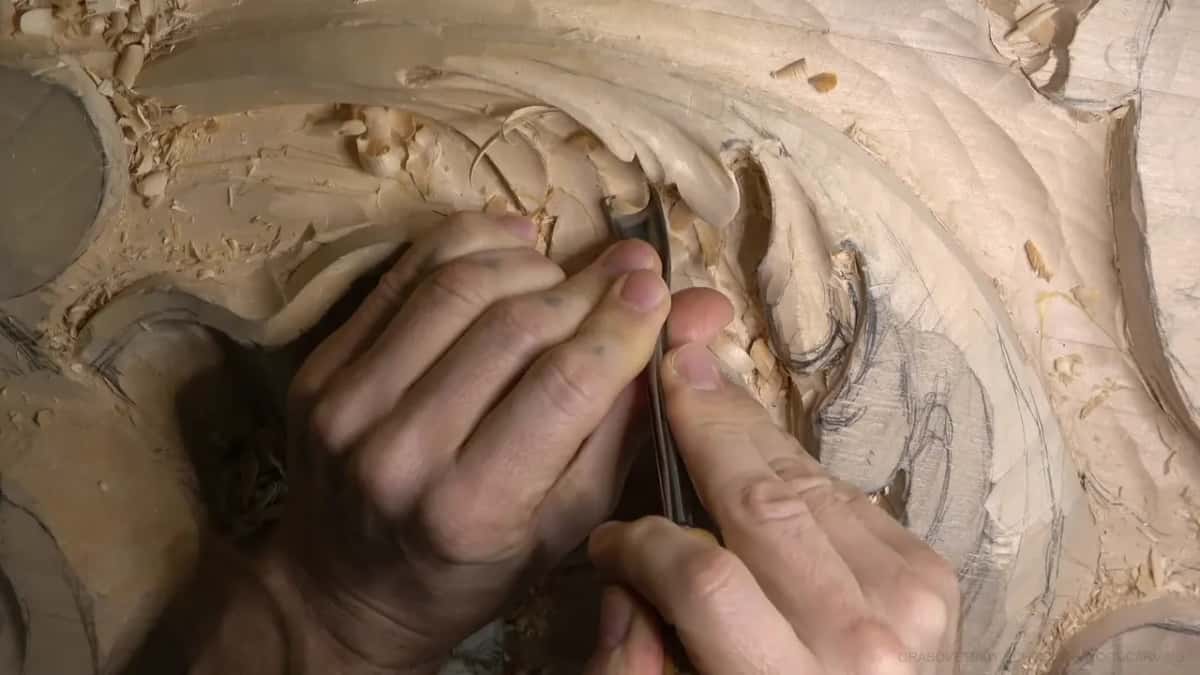 Two hands press a narrow gouge deep into a hollow of the leaf.