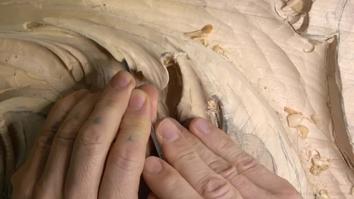 Knuckles rest on the panel as a very small tool slips under one lobe, beneath the curl above.