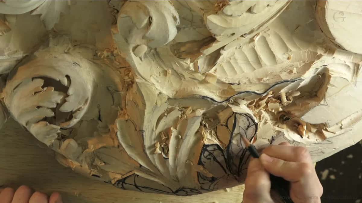 Holding a black marker, he draws curved division lines low on the leaf, his other hand at the corner