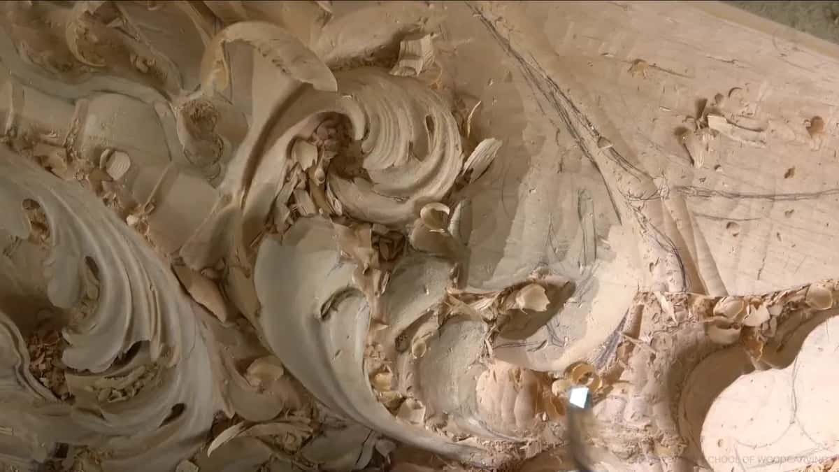 Wide view of the carved board, acanthus scrolls curling across it, chips still lying in the hollows.