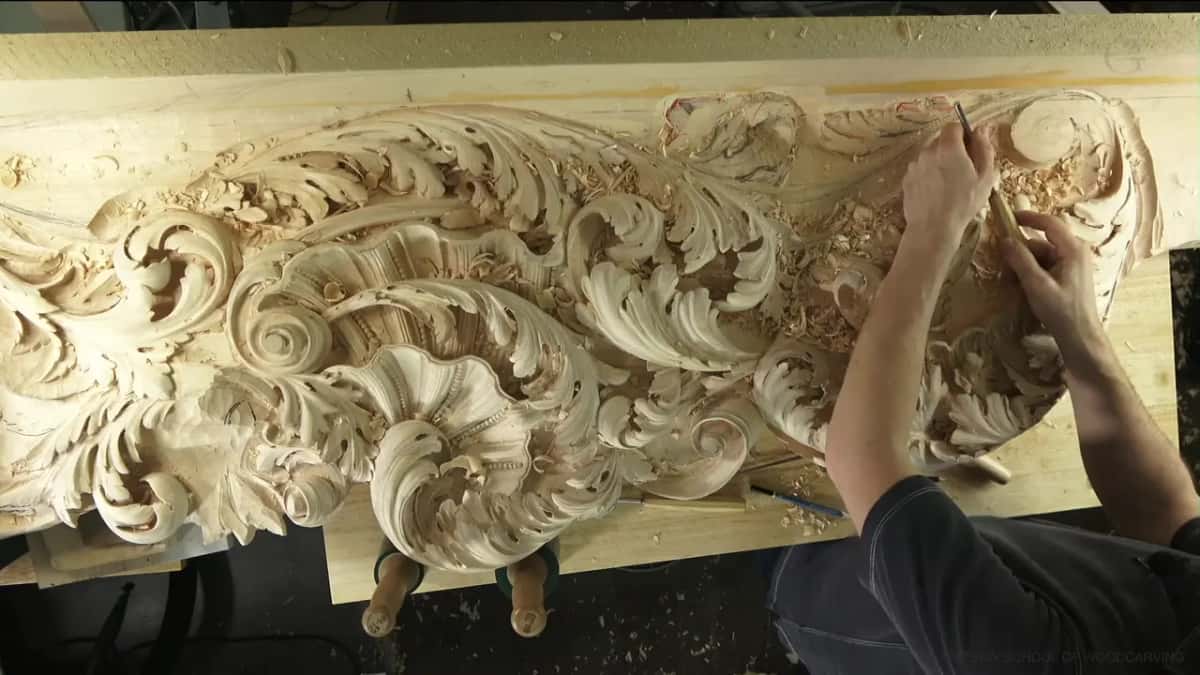 Both hands working the far end of the panel, two mallet handles lying on the bench below and chips everywhere.
