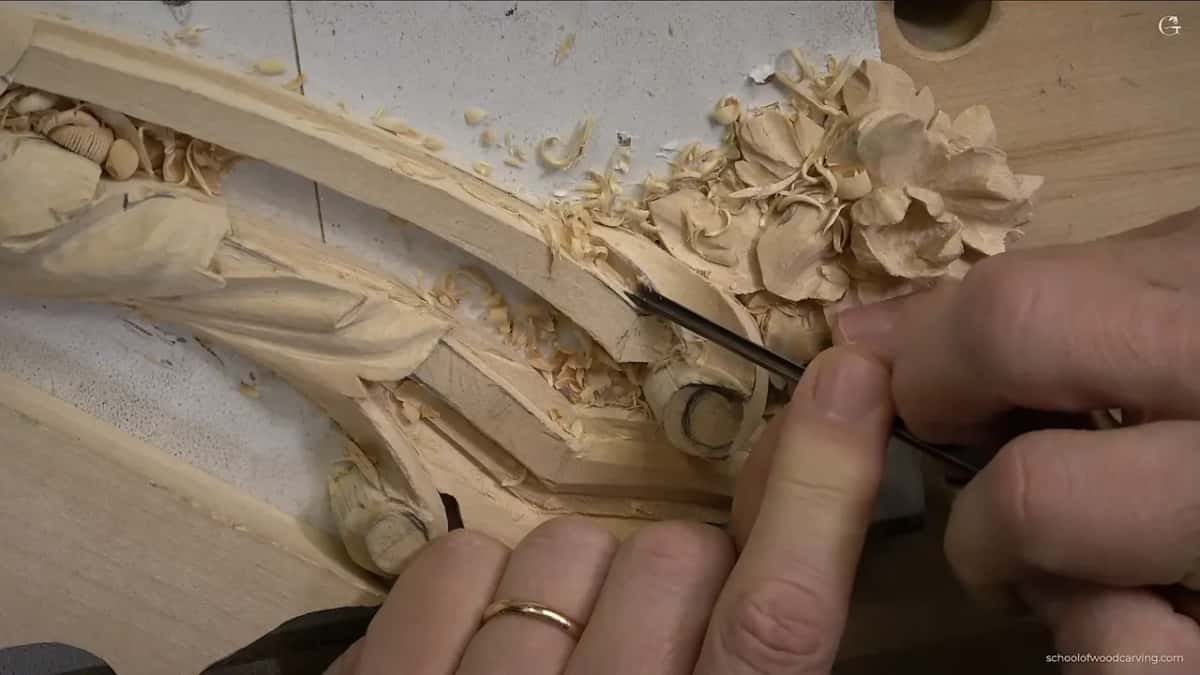 Volute and flower, one hand steadying the whole panel while the other works.