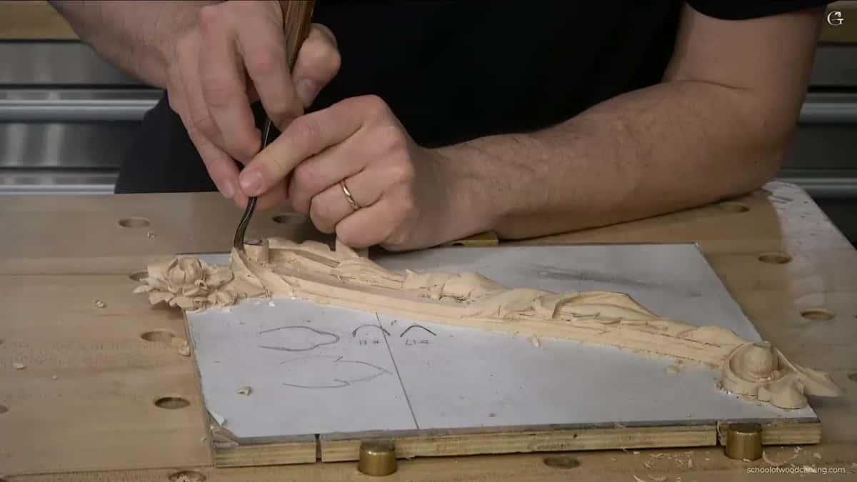 Hands over the pencil drawing, the finished half of the panel beside the part still to carve.