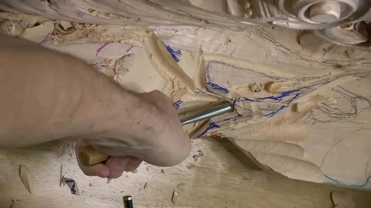An arm leans over the panel, driving a gouge into the wood