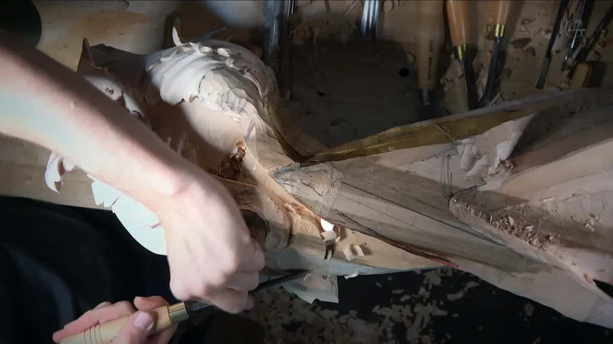 An arm reaches across the leafy head to set a gouge against the scroll