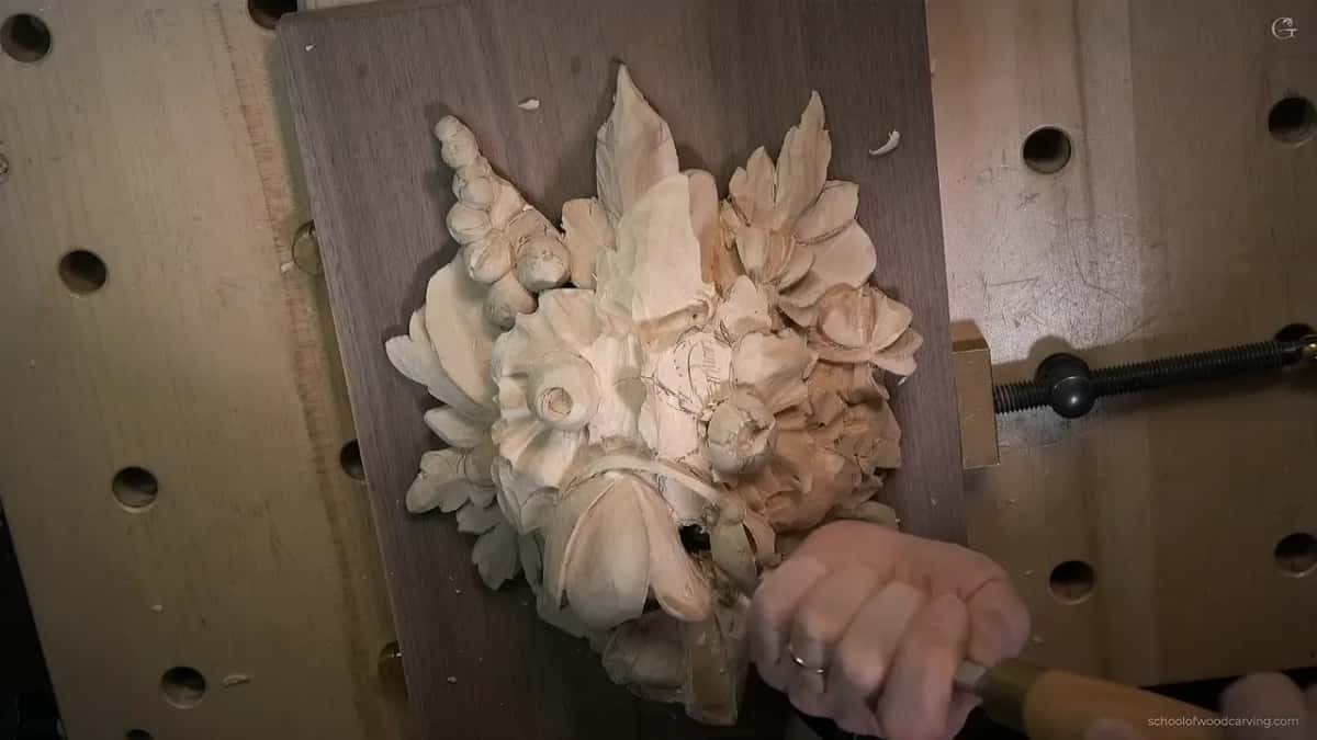 A big skew pressed in at the lower right while the other hand keeps the carving steady on its board