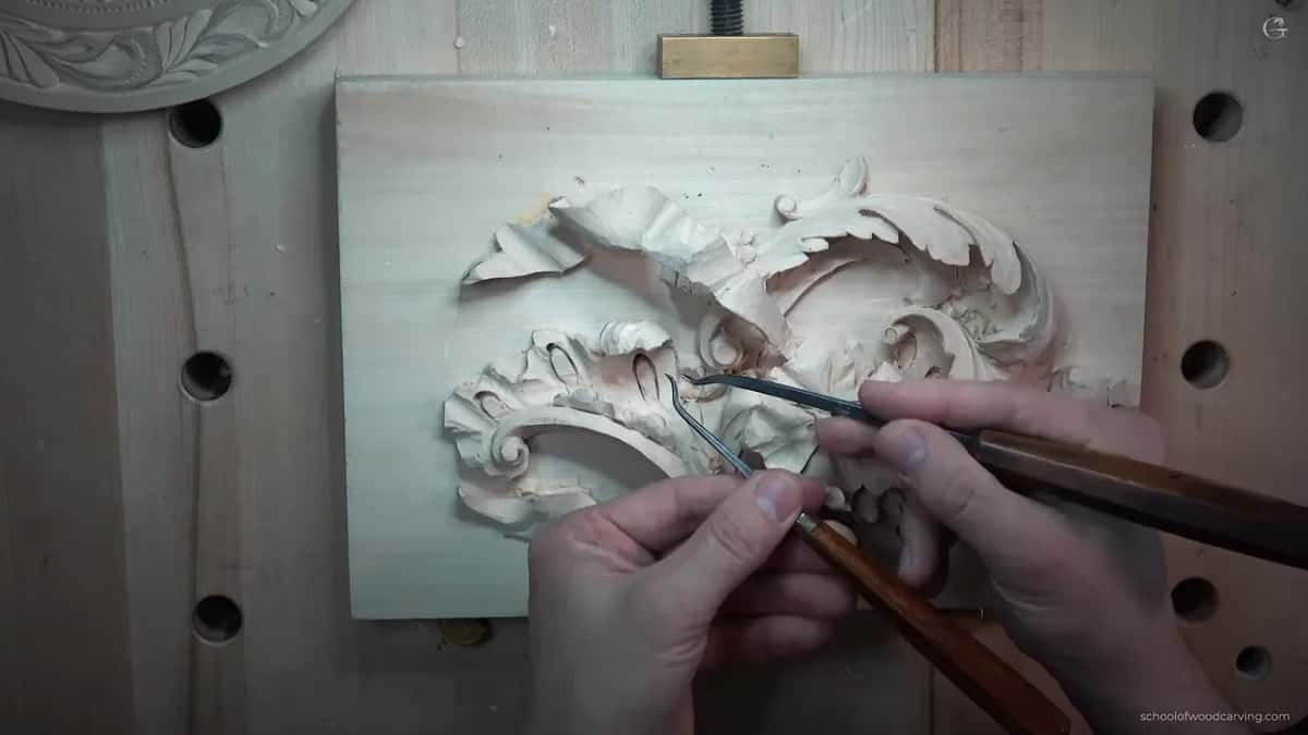 Different bent tool with a dark handle laid across the same carving for comparison.